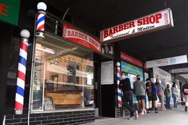 Người dân xếp hàng bên ngoài một tiệm cắt tóc tại Melbourne, Australia. (Ảnh: AFP/TTXVN)