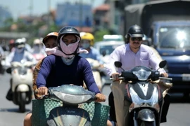 Người dân tìm đủ mọi cách để tránh nắng nóng khi di chuyển trên đường. (Ảnh: Quang Quyết/TTXVN)