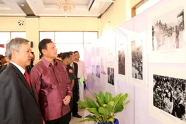 Đại sứ Nguyễn Mạnh Hùng và Bí thư, Tỉnh trưởng Savannakhet, ông Santiphap Phomvihane cùng các quan khách đang đi xem ảnh trưng bày tại triển lãm. (Ảnh: Phạm Kiên/Vietnam+)