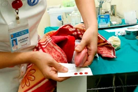 Lấy máu gót chân để tầm soát các bệnh cho trẻ sơ sinh. (Ảnh: Dương Ngọc/TTXVN)