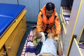 Các y, bác sỹ Trung tâm Phối hợp tìm kiếm cứu nạn hàng hải Việt Nam sơ cấp cứu cho thuyền viên Phạm Văn Thảo trước khi đưa vào đất liền. (Ảnh: Tá Chuyên/TTTXVN)