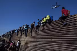 Người di cư Trung Mỹ tìm cách vượt qua hàng rào chắn tại khu vực biên giới ở Tijuana, bang Baja California (Mexico), trong hành trình tới Mỹ. (Nguồn: AFP/TTXVN)