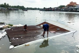 Người dân tháo dỡ tài sản bị chìm dưới sông do sạt lở. (Ảnh: Thanh Liêm/TTXVN)