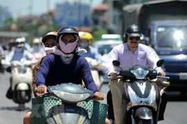 Người dân tìm đủ mọi cách để tránh nắng nóng khi di chuyển trên đường. (Ảnh: Quang Quyết/TTXVN)