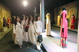 Các em học sinh xem các mẫu áo dài tại triển lãm. (Ảnh: Quang Nhựt/TTXVN)