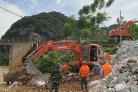 Ủy ban Nhân dân huyện Con Cuông huy động phương tiện, lực lượng khẩn cấp cứu cây cầu. (Ảnh: TTXVN)