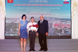 Bà Ivana Belcáková, Đại biện lâm thời Đại sứ quán Cộng hòa Slovakia tại Việt Nam tặng hoa vinh danh ông Trần Xuân Đàm (giữa), người đã tham gia biên soạn cuốn Từ điển Tiệp Khắc-Việt Nam. (Ảnh: Xuân Khu/TTXVN)