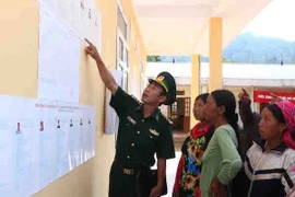Bộ đội biên phòng Đồn Ka Lăng hướng dẫn cử tri bản Tá Bạ tìm hiểu danh sách cử tri. (Ảnh: Quý Trung/TTXVN) 