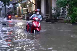Người dân phải dắt xe bị chết máy qua dòng nước ngập trên đường Phú Thuận (Quận 7). (Ảnh: TTXVN phát)