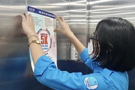 Đoàn viên thanh niên tình nguyện dán tờ rơi tuyên truyền phòng, chống dịch COVID-19 tại thang máy một khu chung cư trên địa bàn quận 1. (Ảnh: Hồng Giang/TTXVN)