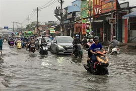 Người dân vất vả di chuyển giữa dòng nước ngập trên Quốc lộ 30, huyện Bình Chánh. (Ảnh: Thanh Vũ/TTXVN)