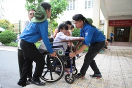 Thí sinh khuyết tật Lê Thị Hà An được các bạn sinh viên tình nguyện nhiệt tình hỗ trợ đến dự thị. (Ảnh: Minh Sơn/Vietnam+)