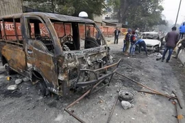 Mọi người đứng cạnh các phương tiện bị người biểu tình đốt cháy trong cuộc biểu tình, sau khi Quốc hội thông qua Dự luật sửa đổi công dân (CAB), tại Guwahati, ngày 13/12. (Nguồn: Reuters)