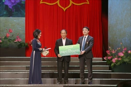Ông Nghiêm Xuân Thành - Chủ tịch HĐQT Vietcombank trao biển tượng trưng tặng thuyền máy cho ông Võ Văn Bình và học bổng cho cháu Võ Nhật Thanh. (Ảnh: Vietnam+)