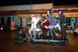 Nhiều xe ba gác máy vận chuyển xe máy của người dân qua điểm ngập sâu. (Ảnh: Mạnh Linh/TTXVN) 
