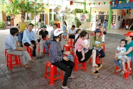 Nhiều phụ huynh ôm con ngồi sân trường bức xúc vì con mình không được nhận vào lớp học. (Ảnh: Phan Quân/TTXVN)