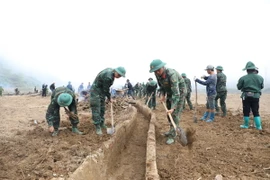 Các chiến sỹ thuộc Trung đoàn 82, nạo vét kênh mương, thu gom đất đá giúp người dân vùng lũ Mường Pồn sớm khôi phục sản xuất. (Ảnh: Phan Quân/TTXVN)