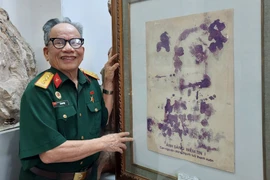 Họa sỹ Lê Duy Ứng và phiên bản của bức chân dung Bác Hồ vẽ bằng máu. (Ảnh: Minh Thu/Vietnam+)