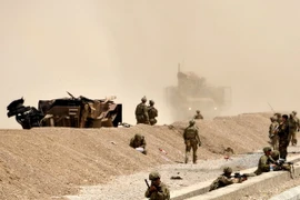 Binh sỹ Mỹ gác tại hiện trường, bên chiếc xe hộ tống bị phá hủy sau vụ tấn công ở Kandahar ngày 2/8. (Nguồn: EPA/TTXVN)