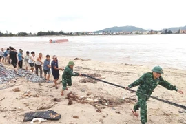 Cán bộ, chiến sỹ Đồn Biên phòng Cửa khẩu Cảng Gianh (Bộ đội Biên phòng Quảng Bình) và người dân cùng các lực lượng liên quan triển khai các biện pháp cứu hộ tàu cá bị lật. (Ảnh: TTXVN phát)