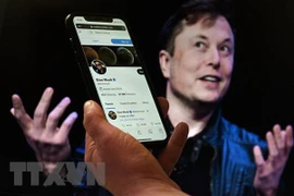 Tài khoản Twitter của tỷ phú Elon Musk trên màn hình điện thoại và ảnh chụp ông Musk (phía sau) . (Ảnh: AFP/TTXVN)