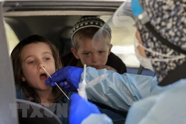 Nhân viên y tế lấy mẫu xét nghiệm COVID-19 cho một em nhỏ tại Berlin. (Ảnh: AFP/TTXVN)