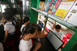 Các em học sinh trường Tiểu học Him Lam (thành phố Vị Thanh, tỉnh Hậu Giang) đọc sách, báo tại Xe thư viện lưu động đa phương tiện. (Ảnh: Duy Khương/TTXVN)