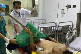 Nạn nhân nhập viện vẫn dính dao cạo mủ cao su có đoạn tay cầm khoảng 1m. (Nguồn: thanhnien.vn)