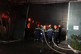 Lực lượng chức năng nỗ lực để đám cháy không lan sang các nhà kho khác liền kề. (Ảnh: Đỗ Trưởng/TTXVN)