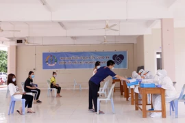 Các sinh viên Việt Nam nộp giấy khai tên họ, số điện thoại và khai lịch sử đi lại cho các nhân viên y tế Lào trước khi lấy mẫu xét nghiệm. (Ảnh: Phạm Kiên/Vietnam+)