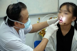 Bác sỹ thăm khám và cắt chỉ vết thương cho bé Đ.L.P.T. (Ảnh: Phương Vy/TTXVN)