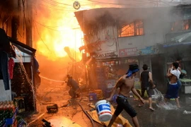 Nhân viên cứu hỏa và người dân địa phương nỗ lực khống chế một đám cháy tại khu dân cư nghèo ở khu vực ngoại ô thủ đô Manila. (Ảnh: AFP/TTXVN)
