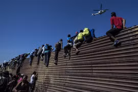 Người di cư vượt qua bức tường biên giới Mỹ-Mexico ở gần cửa khẩu El Chaparral, Tijuana, bang Baja California, Mexico. (Ảnh: AFP/TTXVN)