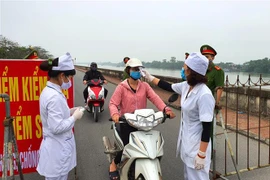 Đo thân nhiệt người qua lại khu đường đê ven sông Đào thành phố Nam Định. (Ảnh: Công Luật/TTXVN)