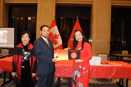Giáo sư Julie Nguyễn (áo đỏ) tặng Đại sứ Việt Nam tại Canada Phạm Cao Phong và phu nhân hai tác phẩm "Bài ca Hồ Chí Minh" và "Lời ru nước Việt" mà giáo sư vừa ra mắt. (Ảnh: Vũ Quang Thịnh/TTXVN)