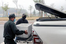 Nhân viên chốt kiểm dịch hỗ trợ người dân đưa nhu yếu phẩm vào vùng phong tỏa. (Ảnh: Văn Đức/TTXVN)