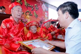 Đại diện Ban Tổ chức trao giấy mừng tho cho các cụ. (Ảnh: Phạm Kiên/Vietnam+)