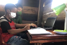 Thiếu tá Lê Anh Tuấn, Đội tổng hợp Công an huyện Cư M’Gar hướng dẫn học sinh có hoàn cảnh khó khăn sử dụng laptop do anh trao tặng. (Ảnh: TTXVN phát)