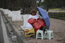 Người bán vé số mặc áo mưa để tránh gió rét. (Hà My/TTXVN)