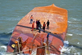 Lực lượng cứu hộ tiến hành móc cáp vào thân tàu Hoàng Phúc 18 để triển khai công tác trục vớt. (Ảnh: TTXVN)