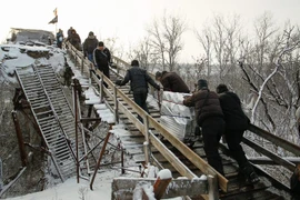 Người dân đi qua chốt kiểm soát giữa quân đội Ukraine và lực lượng đòi độc lập bằng chiếc thang gỗ thay thế cho chiếc cầu bị phá hủy trong một đợt giao tranh ở khu vực Luhansk ngày 16/12. (Nguồn: EPA/TTXVN)