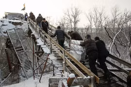 Người dân đi qua chốt kiểm soát giữa quân đội Ukraine và lực lượng đòi độc lập bằng chiếc thang gỗ thay thế cho chiếc cầu bị phá hủy trong một đợt giao tranh ở khu vực Luhansk ngày 16/12. (Nguồn: EPA/TTXVN)