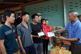 Chủ tịch Hội người Việt Nam tại tỉnh Attapeu Võ Văn Mừng trao tặng số tiền 1 triệu Kip cho 3 gia đình bị ảnh hưởng sau sự cố vỡ đập thủy điện Xe Pian-Xe NamNoy. (Ảnh: Quang Thái/TTXVN)
