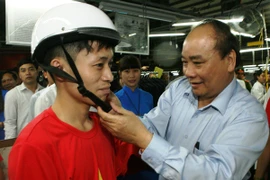 Phó Thủ tướng Chính phủ Nguyễn Xuân Phúc đội mũ bảo hiểm đạt chuẩn cho công nhân Xí nghiệp may 888. (Ảnh: Huy Hùng/Vietnam+)