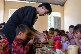 Ca sỹ Đen Vâu cẩn thận bóc tôm cho học sinh vùng cao trong bữa ăn bán trú. (Ảnh: PV/Vietnam+)