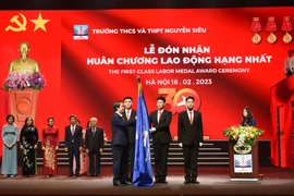 Bộ trưởng Bộ Giáo dục và Đào tạo Nguyễn Kim Sơn thực hiện nghi thức gắn huân chương lên lá cờ truyền thống của trường Nguyễn Siêu. (Ảnh: CTV/Vietnam+)