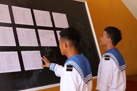  Hai chiến sỹ trẻ lần đầu tiên được đi bầu, theo dõi danh sách cử tri được niêm yết tại Ủy ban Nhân dân xã Song Tử Tây (huyện Trường Sa, tỉnh Khánh Hoà). (Ảnh: Sỹ Tuyên/TTXVN)