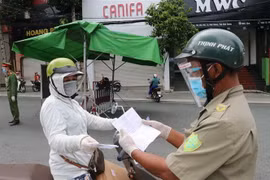 Một người phụ nữ đi chợ trình giấy có giấy tiêm đủ vaccine cho lực lượng kiểm tra trên đường Yersin, thành phố Thủ Dầu Một. (Ảnh: Chí Tưởng/TTXVN)
