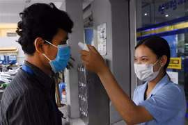 Nhân viên y tế kiểm tra thân nhiệt một khách hàng nhằm ngăn dịch COVID-19 lây lan, bên ngoài một ngân hàng ở Phnom Penh, Campuchia, ngày 17/3/2020. (Ảnh: AFP/TTXVN)