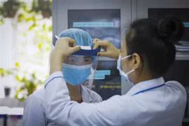 Điều dưỡng trưởng Khoa Khám bệnh-Bệnh viện Đa khoa tỉnh Hòa Bình đội chiếc mũ bảo hộ ngăn giọt bắn cho một đồng nghiệp trong khoa. (Ảnh: Trọng Đạt/TTXVN)